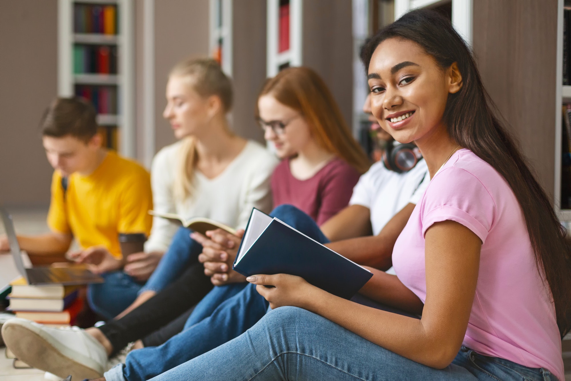 Group of diverse classmates sitting on floor at library